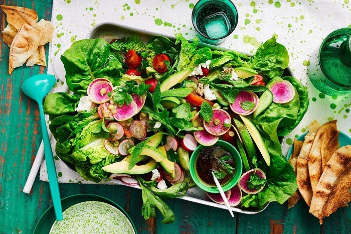 a tray of salad with vegetables and a glass of water