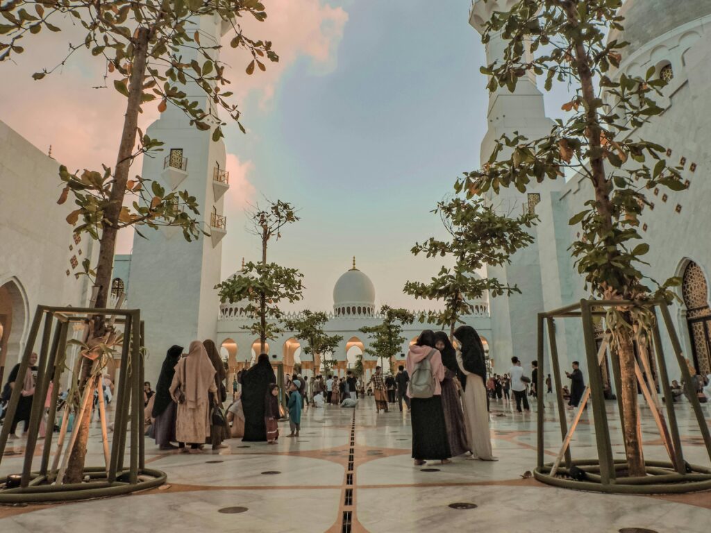 A stunning view of the Sheikh Zayed Grand Mosque during sunset with people gathering under tree-lined pathways.